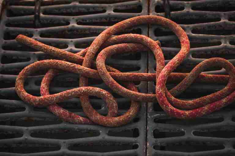 Close-up of a rusty rope coiled on a black industrial grate, showing texture.