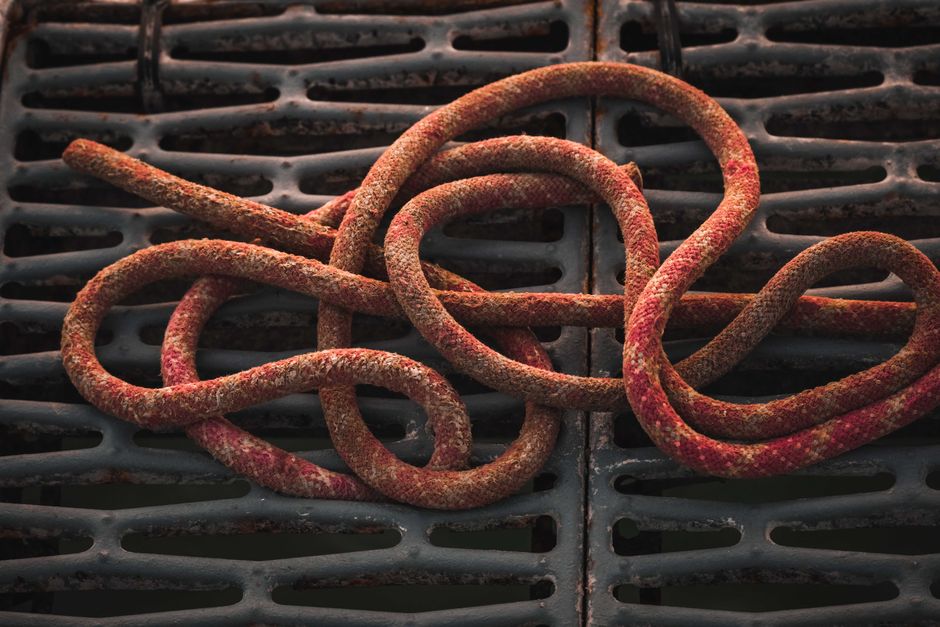 Close-up of a rusty rope coiled on a black industrial grate, showing texture.