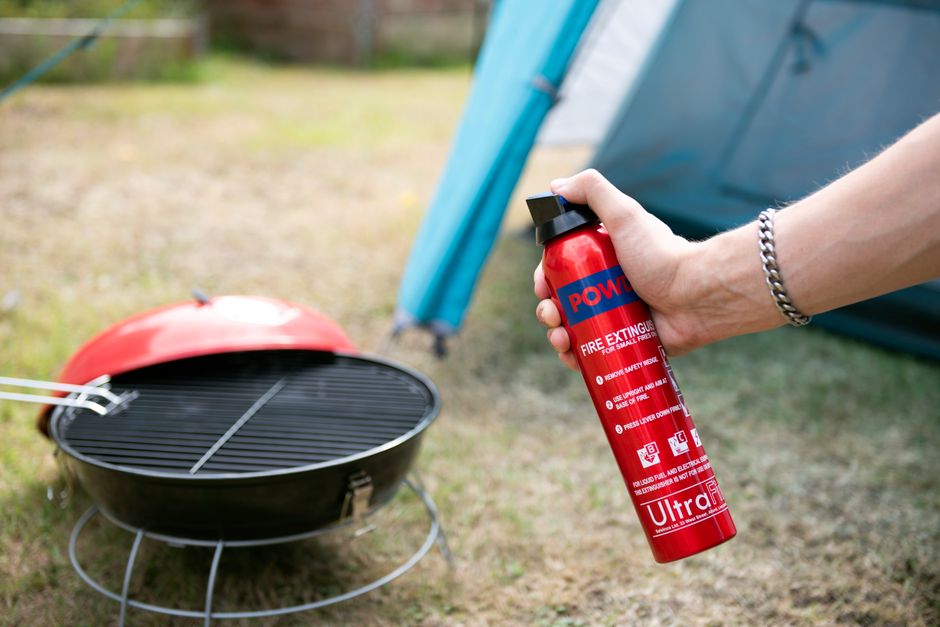 Close-up of hand holding fire extinguisher near a barbecue grill next to a tent.